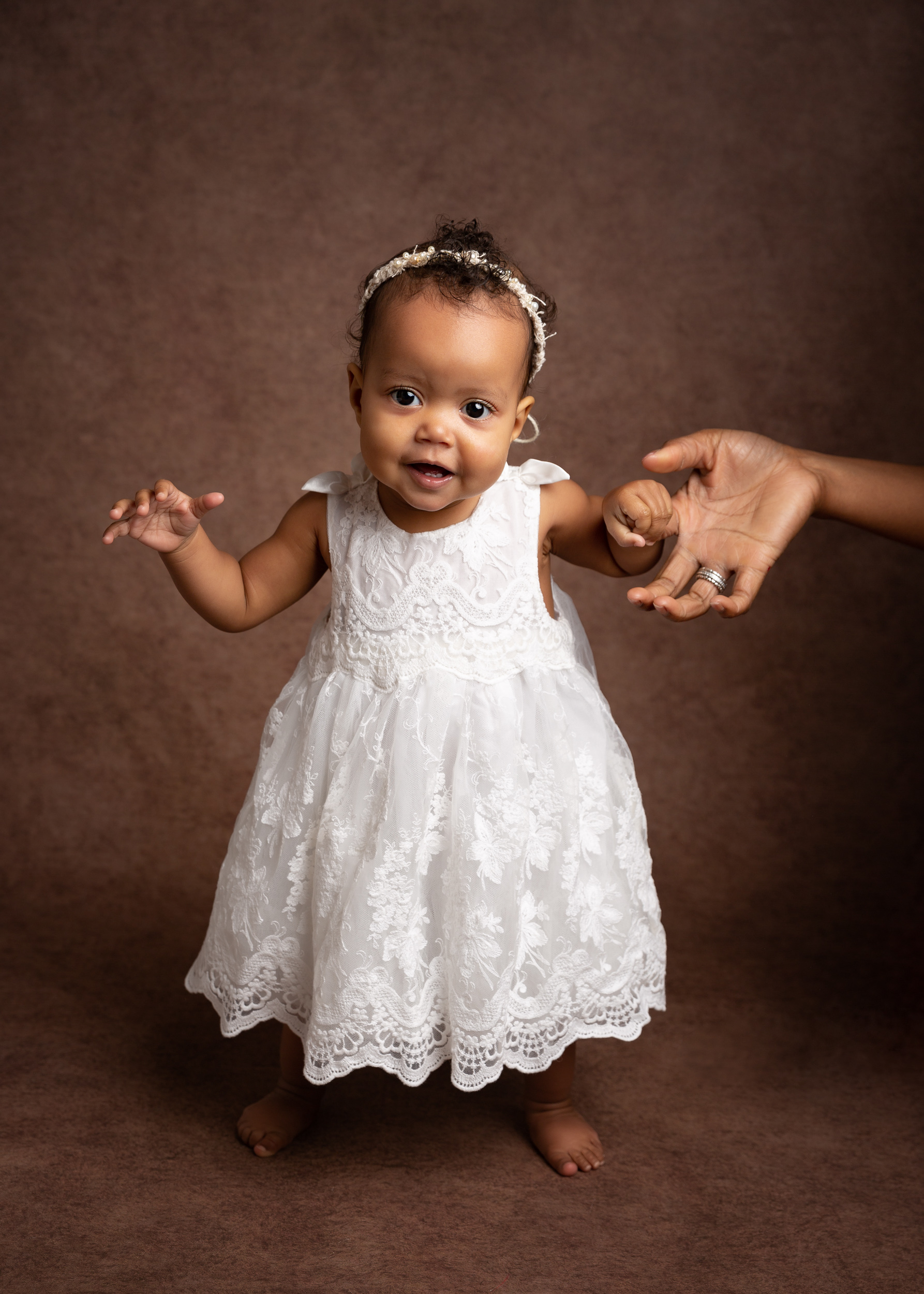 1 year old girl in her special dress holding mummy's hand during her photoshoot in Cheshire