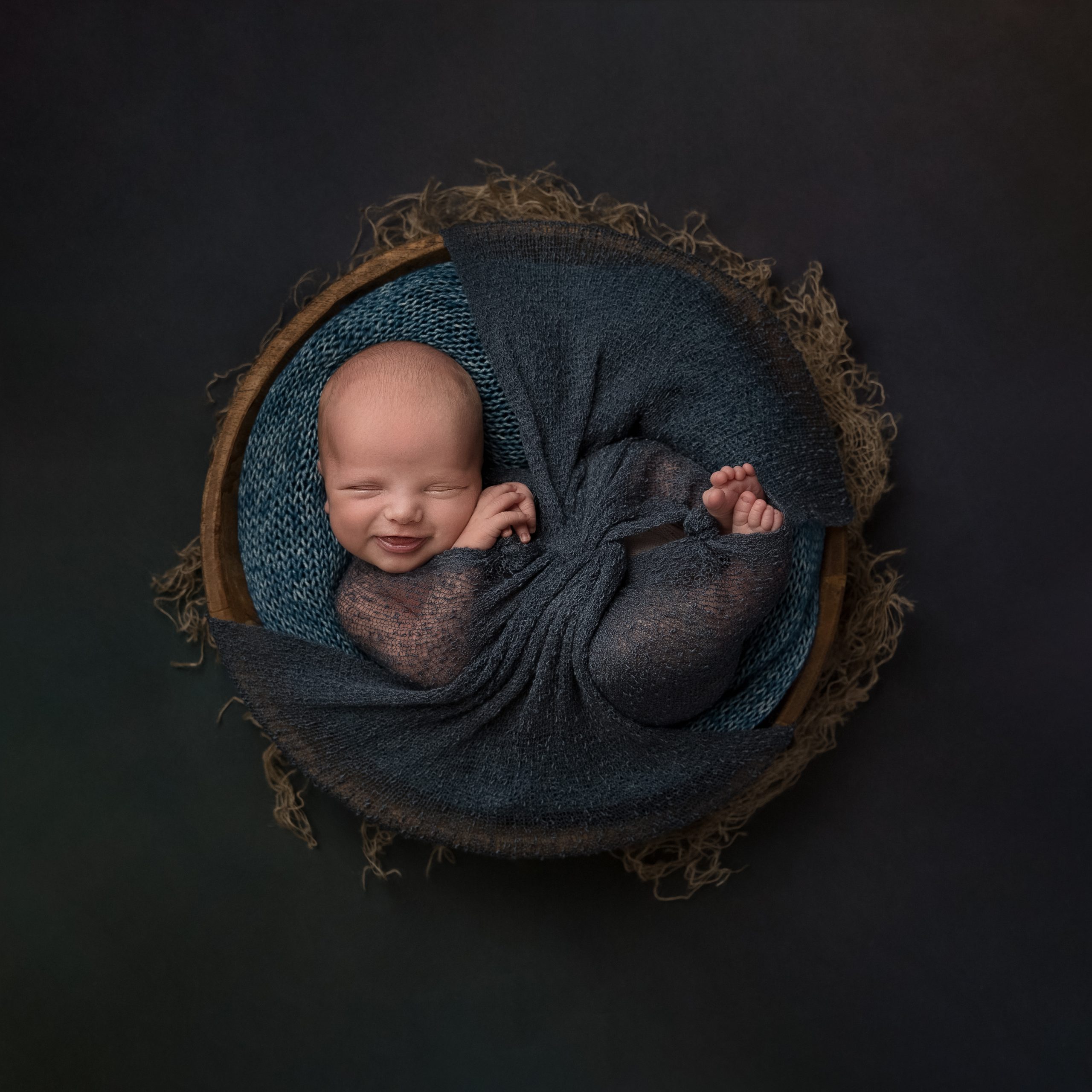 Smiling newborn baby in a bowl as part of my Master Craftsman in Newborn Photography panel by award winning photographer