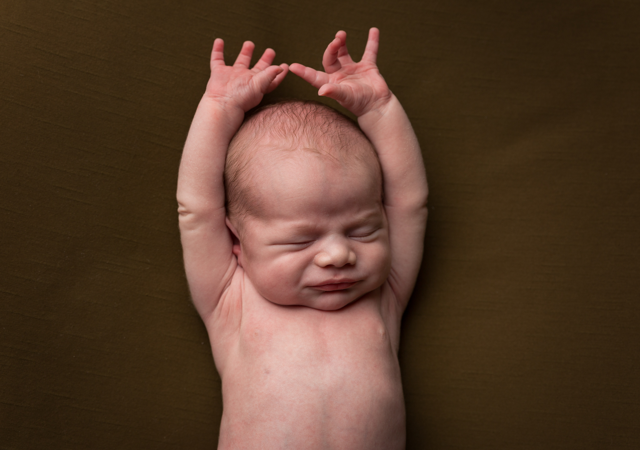 Relaxed posed newborn baby stretching his arms up by Cheshire newborn photographer in Sandbach
