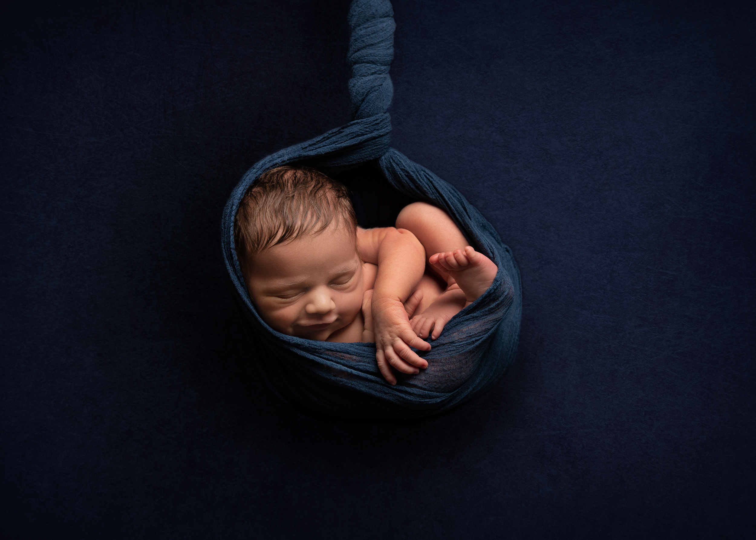 Baby hanging in wrap with blue colour scheme by Cheshire newborn photographer in Sandbach