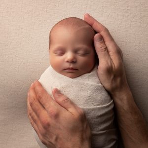 Newborn baby wrapped in white, safe in daddy’s hands by Cheshire newborn photographer in Sandbach