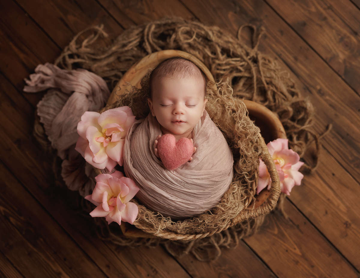 Beautiful newborn baby girl wrapped and posed in wooden prop holding a heart 